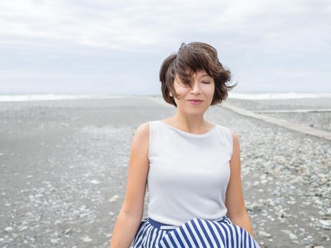 Portrait of smiling woman on seaside. Woman with hair ruffled with the wind. Wanderlust concept. Vacation on sea coast.