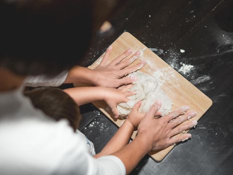 Mother and son are cooking together. Mom and toddler knead dough from flour and eggs on black wooden table. Family time. Fun at kitchen. Developing fine motor skills.