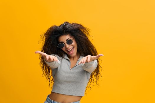 COOL OFFER. I Need You. Cheerful young Latin woman in sunglasses pointing hands at camera over pastel yellow studio wall, free space. Copy space for vacancy concept