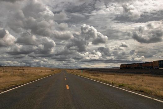 Straight road next to a parallel train under an impressive cloudy sky in route 66 in California USA