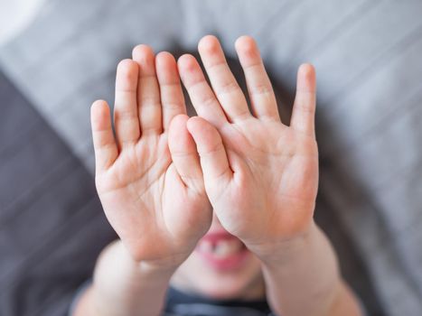 Little boy covers his face with hands. Child refuses to be photographed. Playful kid shows his palm hands instead of laughing face.
