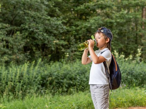 Thirsty boy drinks pure water from reusable green bottle. Summer outdoor recreation. Healthy lifestyle.