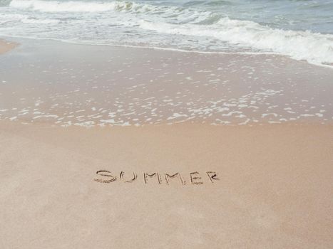 Sea coast with soft surf. Word SUMMER written on sandy beach. Summer vacation on seaside.