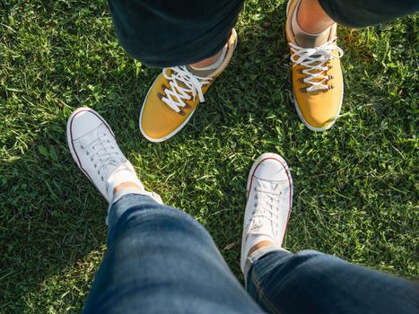 Man and woman stand on green grass lawn in park. Couple on date. Upper view on modern hipster's sneakers. Urban fashion.