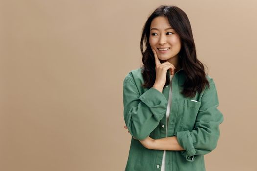 Korean beauty. Happy cheerful Asian student young woman in khaki green shirt recline on hand posing isolated on over beige pastel studio background. Cool fashion offer. Lifestyle and Emotions concept