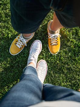 Man and woman stand on green grass lawn in park. Couple on date. Upper view on modern hipster's sneakers. Urban fashion.