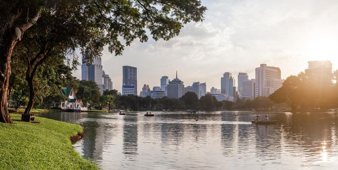 BANGKOK, THAILAND - October 23, 2012. Panorama of downtown skyscrapers from Lumpini park. Sunset view over pond in recreation park.