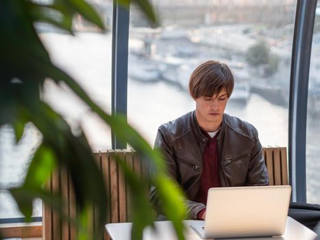 Businessman works with laptop and paper organiser in co-working center. Workplace for freelancers in business center. Sun is shining through panoramic window behind man.