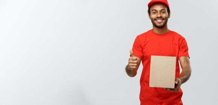 Delivery Concept - Portrait of Happy African American delivery man holding a box package and showing thumps up. Isolated on Grey studio Background. Copy Space