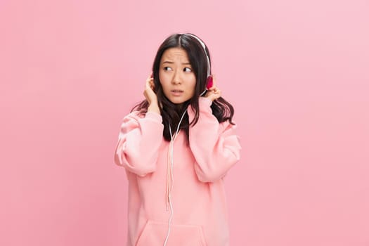 Closeup portrait of shocked cute Asian student young lady in pink hoodie sweatshirt with cute headphones posing isolated on over pink studio background. Good offer. Sound streaming platform ad concept