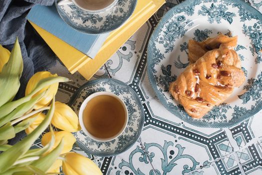 flat lay food, sweet puff, tea in a vintage porcelain cup and a stack of books, a bouquet of yellow withering tulips in a vase,. High quality photo