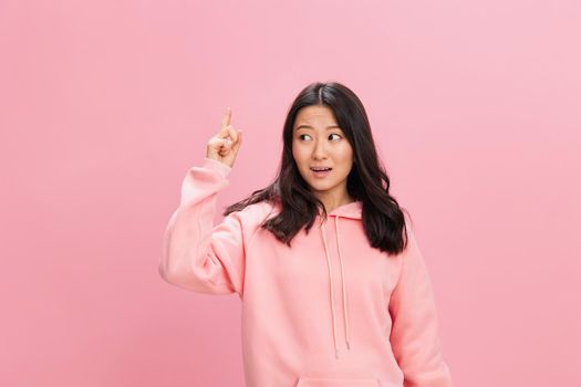 Look Here. Excited Asian student young lady in pink hoodie sweatshirt point finger up posing isolated on over pink studio background. Good offer. Fashion New Collection concept