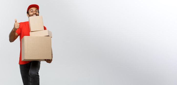 Delivery Concept - Portrait of Happy African American delivery man holding box packages and showing thumps up. Isolated on Grey studio Background. Copy Space