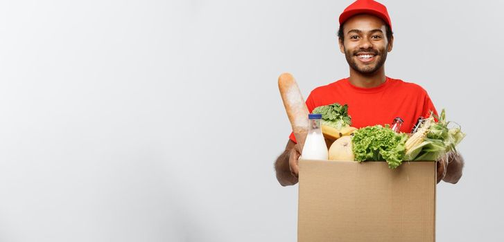 Delivery Concept - Handsome African American delivery man carrying package box of grocery food and drink from store. Isolated on Grey studio Background. Copy Space