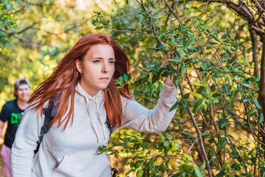 young red-haired woman walking in nature, contemplating the horizon. woman hiker on the road. young people on a trip. background of a lush forest, with green plants illuminated by sun rays.