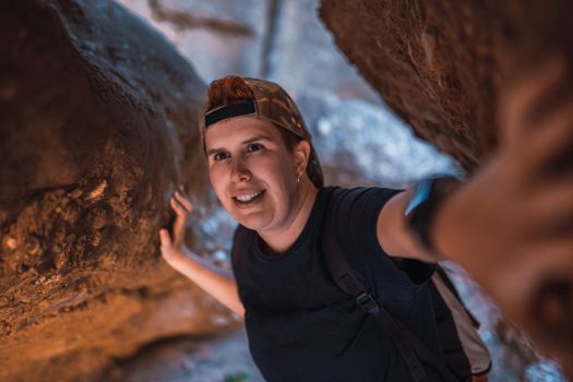 young woman hiking, exploring the entrance of a cave. woman on vacation. young woman hiking in nature. travel person. woman walking in nature. background of a mountain with green plants illuminated by sun rays.