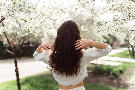 Lovely girl near blooming trees in the park. Outdoor walking in at sunny day. Lifestyle of young woman.