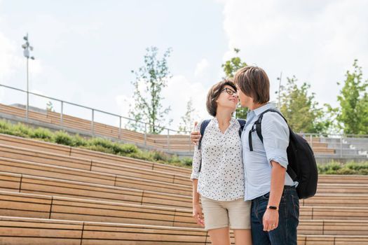 Adult students stand near outdoor audience with wooden seats near university campus. Young couple on romantic date. Summer vibes. Education in Europe.
