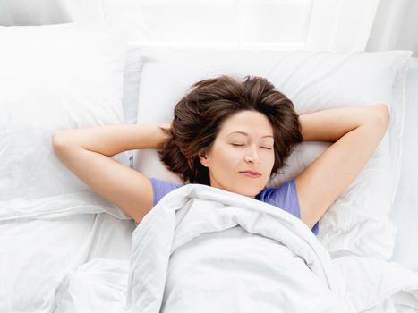 Top view on caucasian woman sleeping in bed. Healthy sleep on white bed linen. Morning at cozy home.