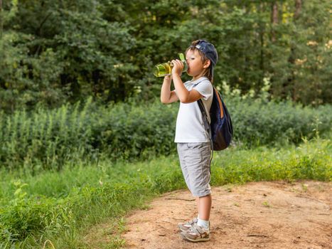 Thirsty boy holds in hands reusable green bottle with pure water. Summer outdoor recreation. Healthy lifestyle.