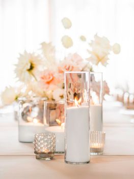 Table set for wedding banquet with burning candles. Floral decorative element - vases with bouquets of pastel colored roses.