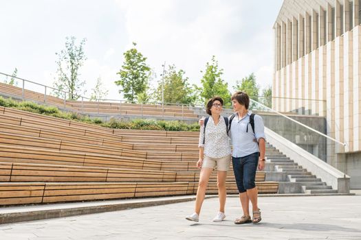 Adult students walk near outdoor audience with wooden seats near university campus. Young couple on romantic date. Summer vibes. Education in Europe.