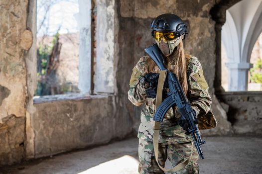 Portrait of a woman in a helmet and goggles with a machine gun in her hands. A female soldier in a camouflage uniform holds a weapon