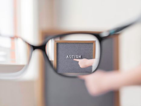 Kid points on grey letterboard with word Autism. View through eyeglasses on medical diagnosis which usually made in childhood. Drawing attention to development of children.