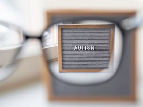 Grey letterboard with word Autism. View through eyeglasses on medical diagnosis which usually made in childhood. Drawing attention to development of children.