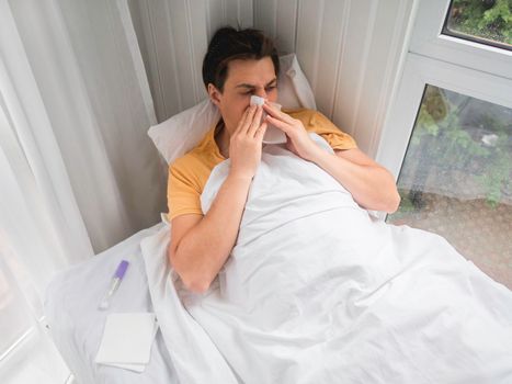 Sick man is lying in bed with thermometer. Man is blowing his nose. Temporary disability in case of disease symptoms.