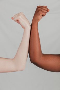 close up fair dark skinned women s hand flexing their fist against grey backdrop