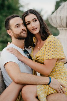 A close photo of a girl in a yellow dress who is sitting on the legs of her boyfriend with a beard on the ancient bridge in old Spain town. A couple of tourists on a date in Valencia.