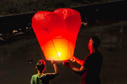 PHUKET, THAILAND - November 28, 2012. Man and boy release heart shaped chinese flying lantern. Father and son on traditional festival Loy Krathong.