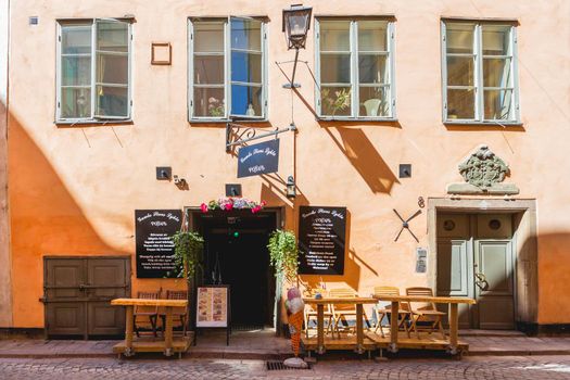 STOCKHOLM, SWEDEN - July 06, 2017. Cafe with open doors and tables outdoors. Sun reflections on bright yellow walls of Gamla stan. Colorful old fashioned buildings in historical part of town.