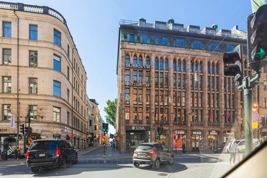 STOCKHOLM, SWEDEN - July 06, 2017. Traffic on Norrlandsgatan street. Cars wait for green traffic light, local people and tourists walk on pavement pass large windows of hotels and stores.