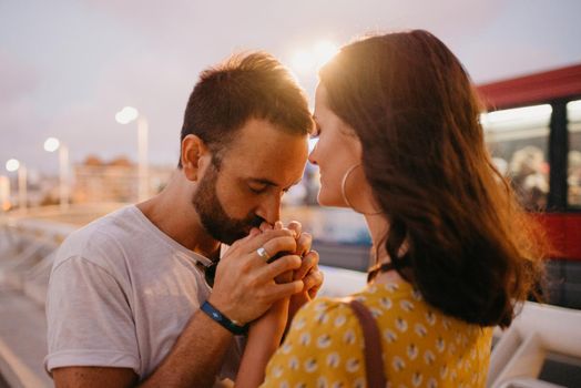 A close photo of a man who is kissing the hands of his girlfriend on a white bridge in Valencia. A couple of tourists on a date in the warm evening.