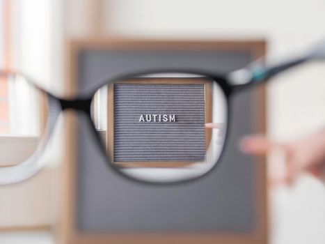 Kid points on grey letterboard with word Autism. View through eyeglasses on medical diagnosis which usually made in childhood. Drawing attention to development of children.