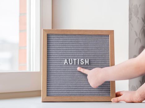 Kid points on grey letterboard with word Autism. Medical diagnosis which usually made in childhood. Drawing attention to development of children.