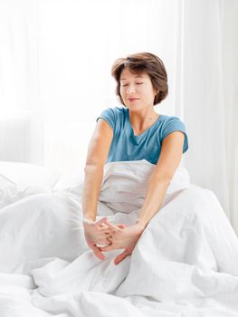 Woman stretches while lying in bed. Pleasant awakening after night's sleep. White bed linen. Top view.