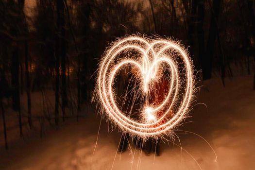 Couple made heart shape with bengal fires. Bright sparkles shines in winter evening. Valentine day celebration. Freeze light.