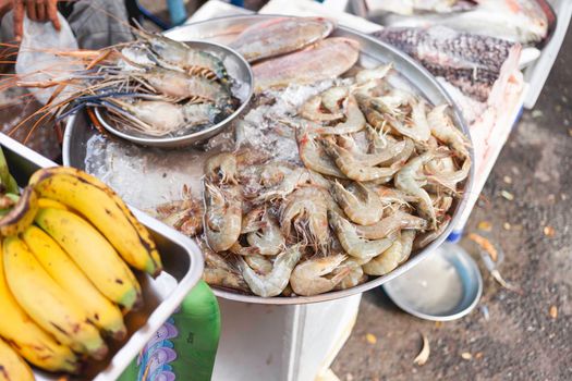 Bananas, fish and shrimps on stall at marketplace. Traditional local fruits and seafood on street market. Bangkok, Thailand.