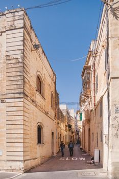 RABAT, MALTA - February 24, 2010. Tourists walk down the narrow street of Rabat. Old buildings with balconies and window shutters.