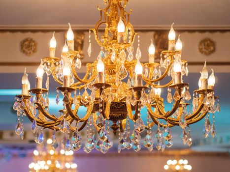 Luxurious retro chandelier with golden swirls and electric light bulbs which looks like candles. Big lamp for large public hall in old fashioned style.