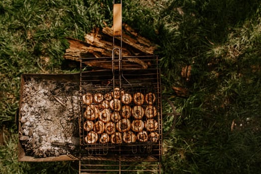 white identical small round mushrooms champignons stacked in even rows in a barbecue on the grill. Green grass background. Summer. White smoke over baked vegetables.