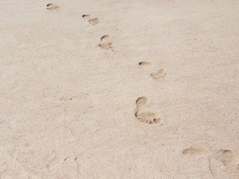 Male footprints on a sandy beach. A chain of bare footprints. Trail to follow. Outline of feet tracks.