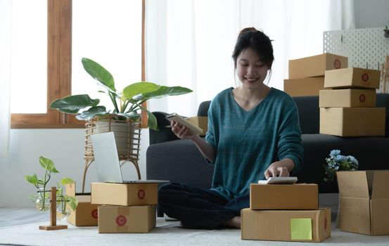 Asian women write note of orders of goods with a smiling face in concept of sme, e-commerce business.