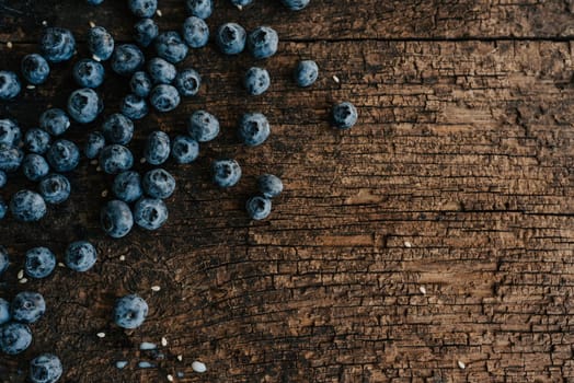 Blue fresh blueberries are scattered on an old brown wooden cracked table. Sesame seeds were poured between the fruits. Wet drops of milk on the table. basil leaves, green fresh seasoning.
