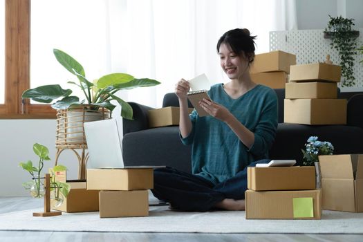 Asian women write note of orders of goods with a smiling face in concept of sme, e-commerce business.