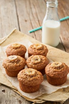 Banana muffin, side view, vertical, copy space. Cupcakes on old linen napkin, rustic wooden table, a breakfast with cake and milk