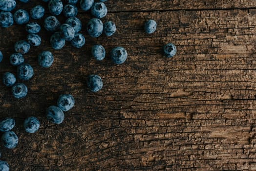 Blue fresh blueberries are scattered on an old brown wooden cracked table.